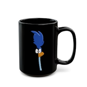 May include: A black ceramic mug featuring a graphic of the Road Runner character. The design shows the bird's head with blue feathers, large white eyes, and an orange beak, positioned on the side of the mug against the solid black background.