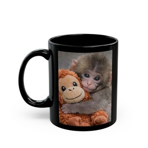Könnte beinhalten: Schwarze Keramik-Tasse mit einem Foto eines Babyaffen, der einen Stoffaffen umarmt. Die Tasse hat einen schwarzen Griff und ein schwarzes Innenleben. Das Bild auf der Tasse ist eine Fotografie des Affen und des Spielzeugs.
