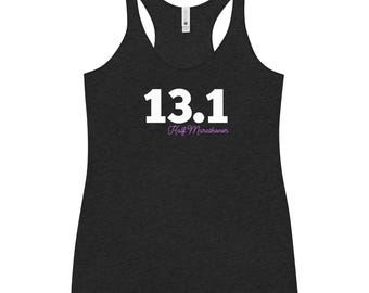 May include: A black racerback tank top with the number "13.1" in white block letters. Below the number, the words "Half Marathoner" are written in a cursive, purple font. The tank top is made of a soft, textured material.