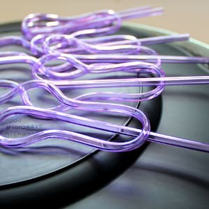 May include: A set of purple plastic drinking straws with a unique looped design. The straws are arranged on a black plate with a silver rim.