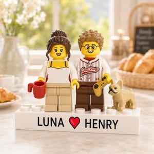 Peut inclure: Deux figurines Lego sur une base rectangulaire blanche avec le texte LUNA, un cœur rouge et HENRY. La figurine de gauche a des cheveux bruns, un haut blanc et une tasse rouge. Celle de droite a des cheveux bruns, des lunettes, un maillot de baseball blanc avec le texte Quacking et une manette de jeu jaune, accompagnée d'un petit bouledogue français beige.