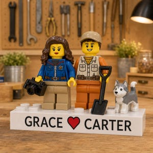 Puede incluir: Dos minifiguras de LEGO sobre una base rectangular blanca con el texto GRACE (símbolo de corazón) CARTER. La figura femenina tiene el pelo largo castaño, chaqueta azul y una cámara negra. La figura masculina lleva gorra beige, chaleco y pantalones naranjas, sosteniendo una pala negra. Un pequeño perro husky gris y blanco está a su lado.