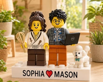Può includere: Un espositore personalizzato con due minifigure in plastica e un piccolo cane bianco su una base rettangolare bianca. La base riporta la scritta SOPHIA, un'icona a forma di cuore rosso e MASON. Una figura indossa una divisa da chef bianca con una frusta, l'altra un gilet grigio e pantaloni arancioni, tenendo in mano un portatile nero.