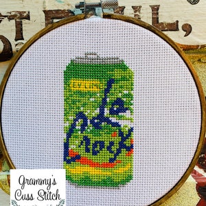 May include: Cross-stitch art of a green soda can with the words "Ade Rocks" in blue and yellow. The artwork is framed in a wooden embroidery hoop. The background is white fabric.