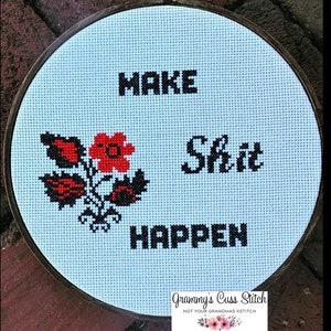 K&ouml;nnte beinhalten: Kreuzstich-Stickerei in einem Holzrahmen mit den Worten "MAKE SHIT HAPPEN" in schwarzen Blockbuchstaben. Ein Blumenmuster in Rot und Schwarz befindet sich auf der linken Seite. Der hellblaue Stoff ist in einem h&ouml;lzernen Stickrahmen befestigt.