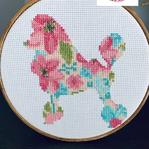 May include: Cross-stitch embroidery of a poodle dog filled with pink, green, and blue floral patterns. The embroidery is set in a wooden hoop. The text "Grammy's Cuss Stitch" is in the upper right corner.