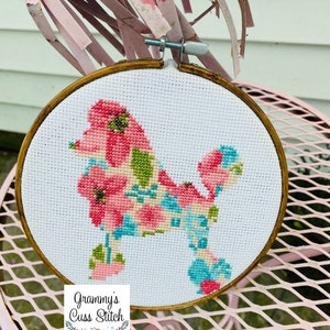 May include: A cross-stitch embroidery hoop featuring a poodle design. The poodle is filled with pink, blue, and green floral patterns. The hoop is set against a white background and framed in a wooden hoop. The text "Grammy's Cuss Stitch" is at the bottom.