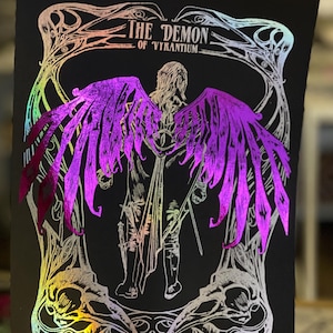 May include: A black and white illustration of a winged figure with the text "THE DEMON OF VYRAINTIUM" above it. The illustration is printed on a black background with a holographic iridescent finish.