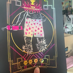 Puede incluir: Impresión artística negra con una figura en pantalones cortos con estampado de corazones, sosteniendo un palo de dinamita rosa. La impresión presenta el texto "NEW ACHIEVEMENT!" y un trofeo dorado. Los pies de la figura están adornados con calzado con púas.