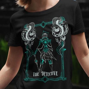 May include: Black t-shirt with a teal graphic design of a person in a cloak holding a staff, surrounded by two snakes. The text "THE DETECTIVE" is below the graphic.
