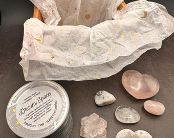 May include: A gift box with tissue paper printed with gold stars and moons. The box contains a candle labeled "Dream Space" and several crystals in various shapes and colors, including a heart and flower.