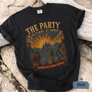 May include: Black t-shirt with a fantasy-themed graphic. The design features the text "THE PARTY RETURNS AT DAWN" above a sunset scene with a castle and figures. Below, it reads "STORIES OF GLORY REMAIN".