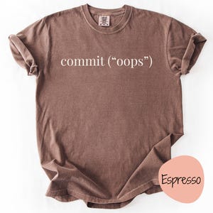 Puede incluir: Camiseta color espresso con la palabra "commit" en blanco, seguida de "(oops)" entre paréntesis. La camiseta tiene cuello redondo y mangas cortas. Un círculo rosa con la palabra "Espresso" está en la esquina inferior derecha.