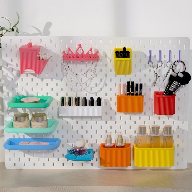 May include: A white pegboard with various colorful organizers. Includes pink, yellow, orange, and red containers for makeup brushes, lipsticks, and skincare products. Also features trays in green and blue, a pink crown, and a small blue decorative dish.