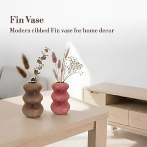 May include: Two ribbed Fin vases, one brown and one pink, on a light wood table. The vases contain dried flowers and grasses. The text reads "Fin Vase" and "Modern ribbed Fin vase for home decor".