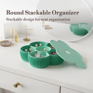 Puede incluir: Un organizador de joyas redondo y apilable, de color verde menta, con diseño de flor. El organizador abierto revela compartimentos llenos de pendientes, anillos y cuentas. La tapa está parcialmente abierta. El texto en la imagen dice "Round Stackable Organizer".