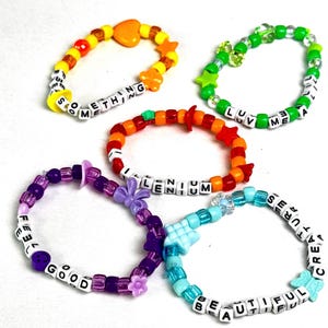 Puede incluir: Cinco pulseras de cuentas de colores con dijes y cuentas de letras que deletrean las palabras "feel good", "something", "millenium", "luv me" y "beautiful creature".