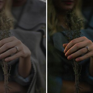 May include: A hand wearing a silver ring with a small gemstone holds dried flowers. The ring is the focal point, set against a blurred background of a person wearing a gray shawl. The image has a soft, natural aesthetic.