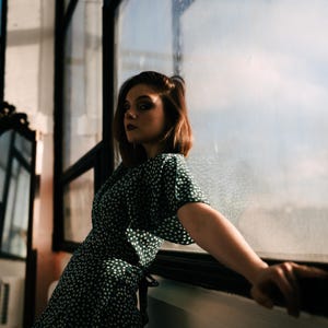 May include: A dark green dress featuring a white polka dot pattern, short sleeves, and a wrap-style front closure. The garment is constructed with a lightweight fabric and displays a consistent print throughout the bodice and sleeve sections.