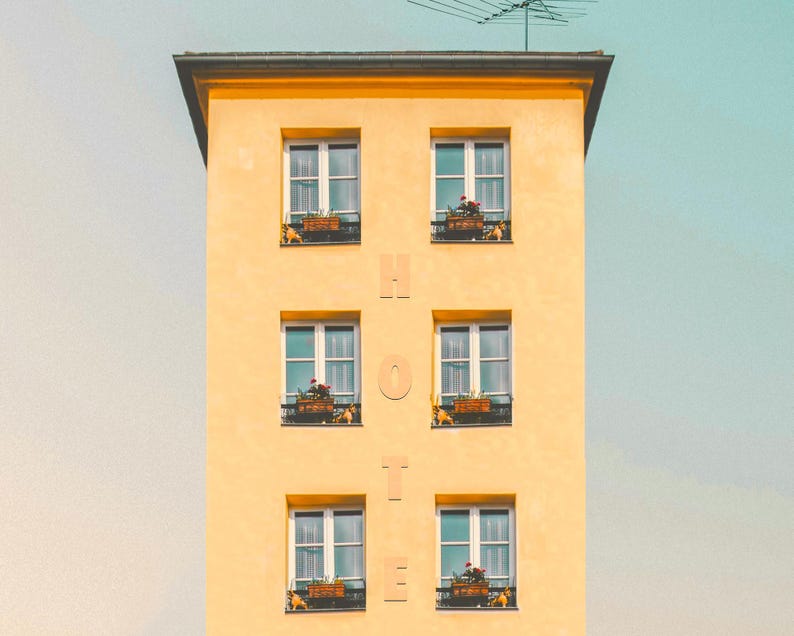 Pu&ograve; includere: Un'alta facciata di edificio gialla con sei finestre disposte in due colonne. Tra le colonne, le lettere H, O, T, E sono allineate verticalmente. Ogni finestra presenta una cornice scura e una fioriera marrone con piccoli fiori rossi.