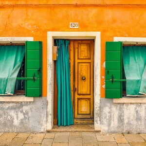Pu&ograve; includere: Una facciata di edificio color arancione brillante con una porta centrale in legno dotata di una tenda color ottanio, affiancata da due finestre con persiane verdi e tende ottanio. Il numero 430 &egrave; visibile sopra la porta, su una base grigia.