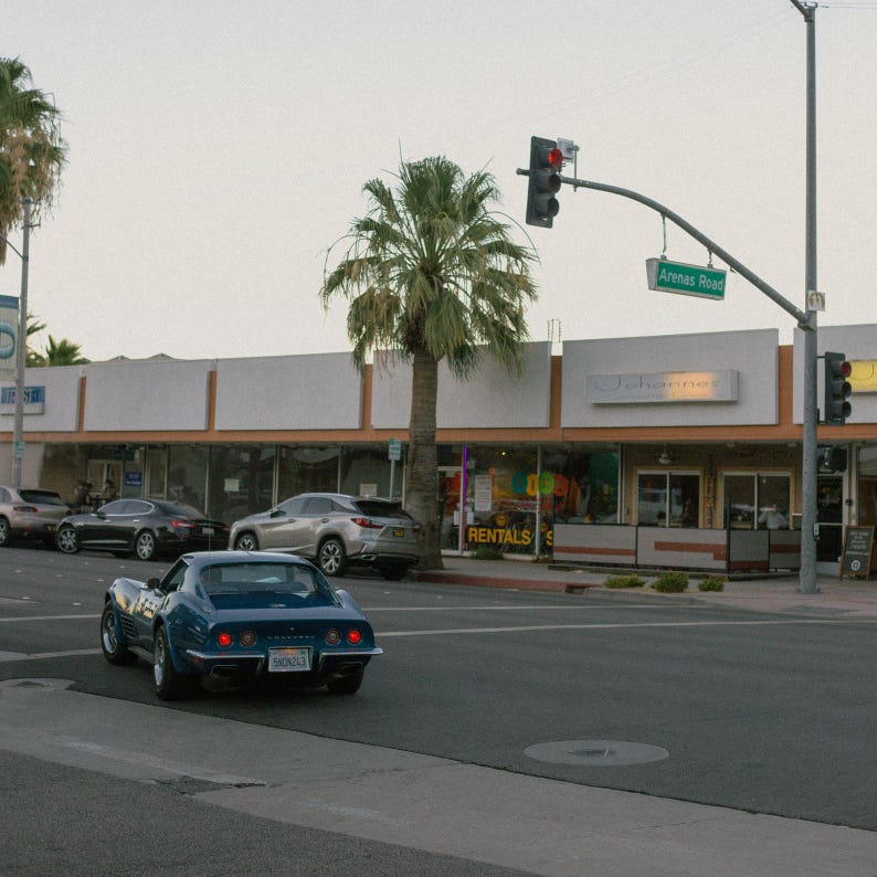 K&ouml;nnte beinhalten: Ein blauer klassischer Chevrolet Corvette Sportwagen, der auf einer Stra&szlig;e vor einem Geb&auml;ude mit einem Schild mit der Aufschrift "Vermietung" geparkt ist.