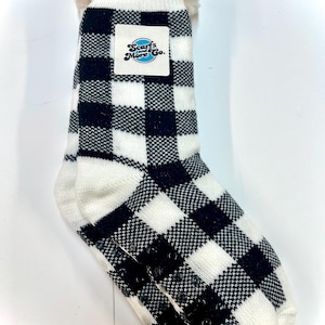 May include: Cozy white and black buffalo check pattern slipper socks with a plush white cuff. The socks have a non-slip grip on the soles and a tag that reads "Scarfs and More Go."