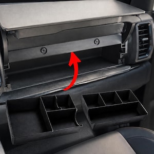 May include: A black plastic glove box organizer insert with multiple compartments for a vehicle dashboard. The organizer is shown positioned below an open glove compartment, with a red arrow indicating the placement of the tray inside the storage area.