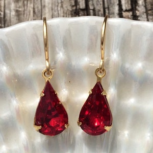 May include: A pair of gold dangle earrings with teardrop-shaped red gemstones.