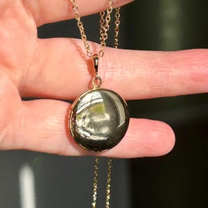 May include: A gold chain necklace with a round gold locket pendant.