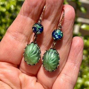 May include: A pair of green and blue glass earrings with a carved design. The earrings are on a gold chain and have a hook closure.