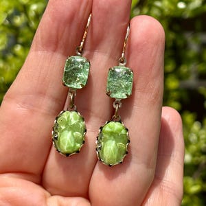 May include: A pair of green glass earrings with a cameo design. The earrings are made of gold-tone metal and have a dangling design.