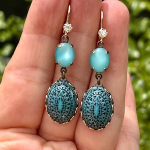 Peut inclure: Boucles d'oreilles en verre bleu turquoise avec un motif gravé détaillé et un accent en cristal transparent en haut.