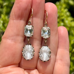 May include: A pair of dangle earrings with two clear crystal stones on each earring. The top stone is a square cut and the bottom stone is oval shaped.