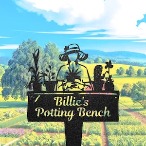 Puede incluir: Estaca de jardín de metal negro con la silueta de una persona con sombrero en un banco de macetas, rodeada de plantas en macetas. El letrero dice "Billie's Potting Bench" en una fuente decorativa, sobre un fondo de campos y cielo azul.