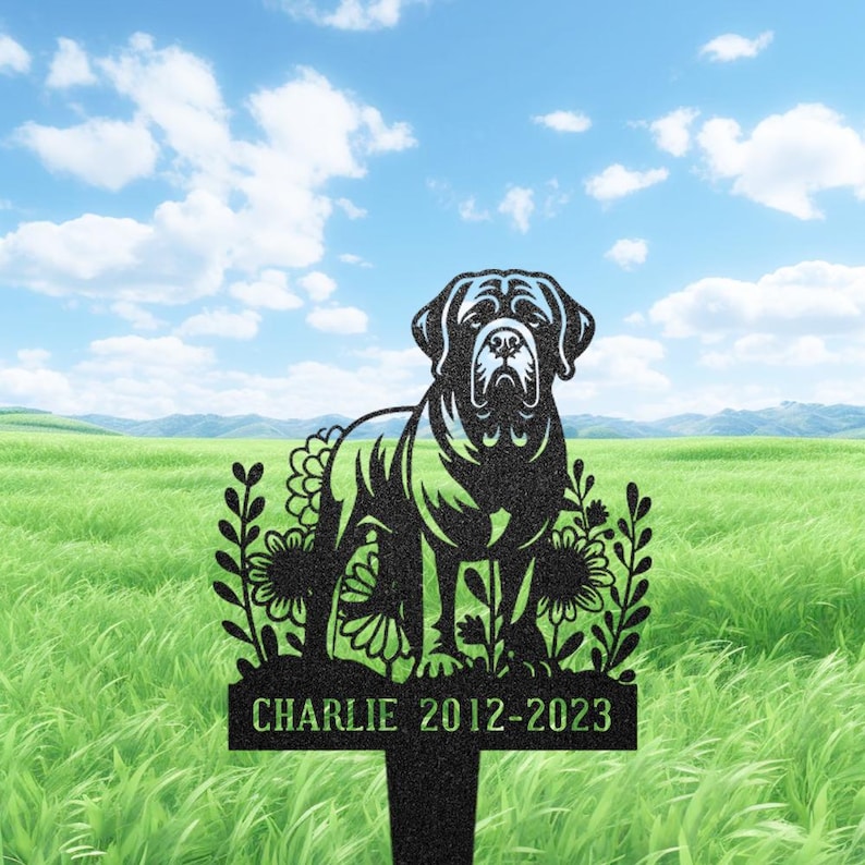 May include: Black metal dog memorial stake featuring a dog silhouette, floral details, and the name "Charlie" with dates "2012-2023". Set against a green field and blue sky, it's a touching tribute.
