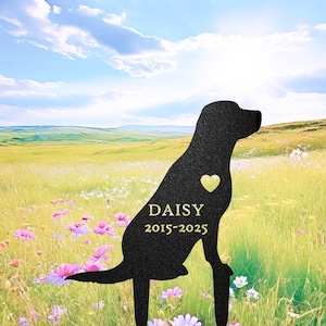 May include: Black metal dog silhouette garden stake with a heart cutout and the name "DAISY" and dates "2015-2025" in gold lettering. The stake is in a field of wildflowers under a blue sky.