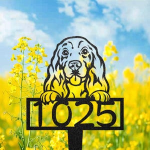 Könnte beinhalten: Schwarzer Metall-Gartenstecker in Hundeform mit der Nummer 1025. Der Hund hat ein detailliertes Gesicht und Pfoten, vor dem Hintergrund gelber Blumen und eines blauen Himmels mit Wolken.