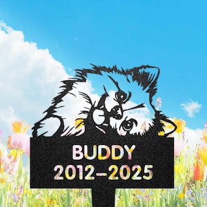 May include: A black metal garden stake with a dog silhouette. The stake displays the name "BUDDY" and the years "2012-2025" in white. The background features a blue sky, clouds, and a field of colorful flowers.