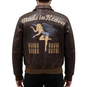 May include: Brown leather jacket with a bomber-style design. The back features a pin-up girl illustration with the text "Made in Heaven" above. Below the illustration are several bomb graphics.
