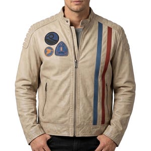 Puede incluir: Chaqueta de cuero color beige con cremallera, rayas azules y rojas en la parte delantera y parches en el hombro izquierdo. La chaqueta tiene cuello alzado y detalles acolchados en los hombros.