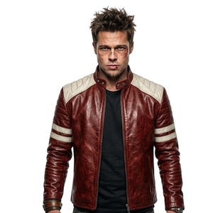 Puede incluir: Una chaqueta de cuero granate con detalles crema en los hombros y rayas blancas en las mangas. La chaqueta tiene un estilo motero clásico con cuello alzado y cremallera frontal. La persona de la imagen lleva una camiseta negra debajo.
