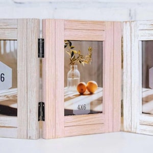 May include: A three-panel wooden picture frame with a distressed white and pink finish. Each panel has a 4x6 inch opening for photos. The frame is hinged and can be folded to display multiple photos.