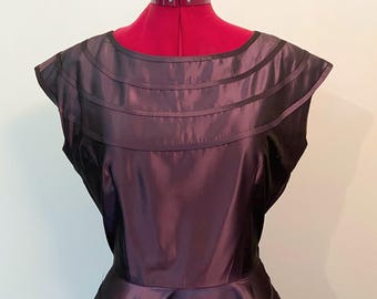May include: A sleeveless, dark purple dress with a fitted bodice and a full skirt. The bodice has a wide, round neckline and is accented with horizontal bands of fabric.