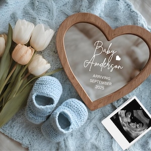 Peut inclure: Un cadre en bois en forme de cœur avec le texte "Baby Anderson Arriving September 2025" est posé sur une couverture en tricot bleu. Des chaussons de bébé en crochet bleu et un bouquet de tulipes sont à côté du cadre. Une image d'échographie est également présente.