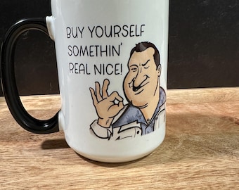 May include: White ceramic mug with a black handle. The mug features a cartoon illustration of a man with a mustache and the text "BUY YOURSELF SOMETHIN' REAL NICE!"