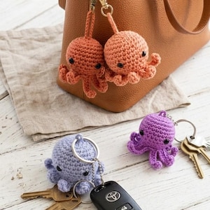 May include: Crocheted octopus keyrings in orange, purple, and blue. The octopus keyrings are attached to keys and a handbag. The keyrings have black eyes and are made of yarn.