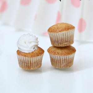 May include: Three miniature cupcakes, one topped with white frosting, are stacked on a white surface. The image includes the text "Miniature food Tutorial" and "1:12th scale miniatures by Tanja Jensen". A pink polka dot background is visible.