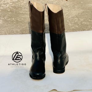 May include: A pair of knee-high boots featuring a two-tone design with black leather lower sections and brown leather upper shafts. The boots have a rounded toe, a low heel, and a light-colored interior lining. The Athletigo Enterprises logo is visible.