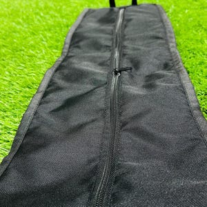 May include: Black, rectangular carrying case with a full-length zipper. The case has a handle at the top and is made of a textured, durable fabric. The zipper is black and runs down the center of the case.